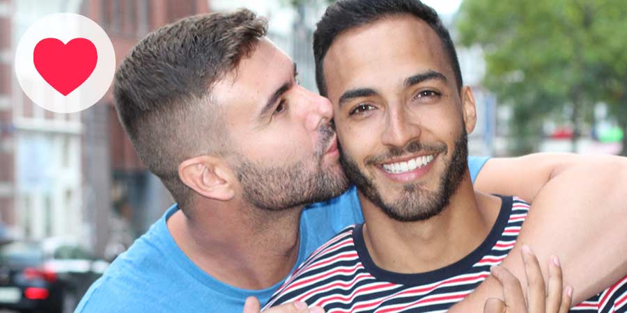 Handsome gay man kissing another man on the cheek.