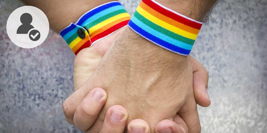 Two men wearing LGBTQ wrist bands holding hands.